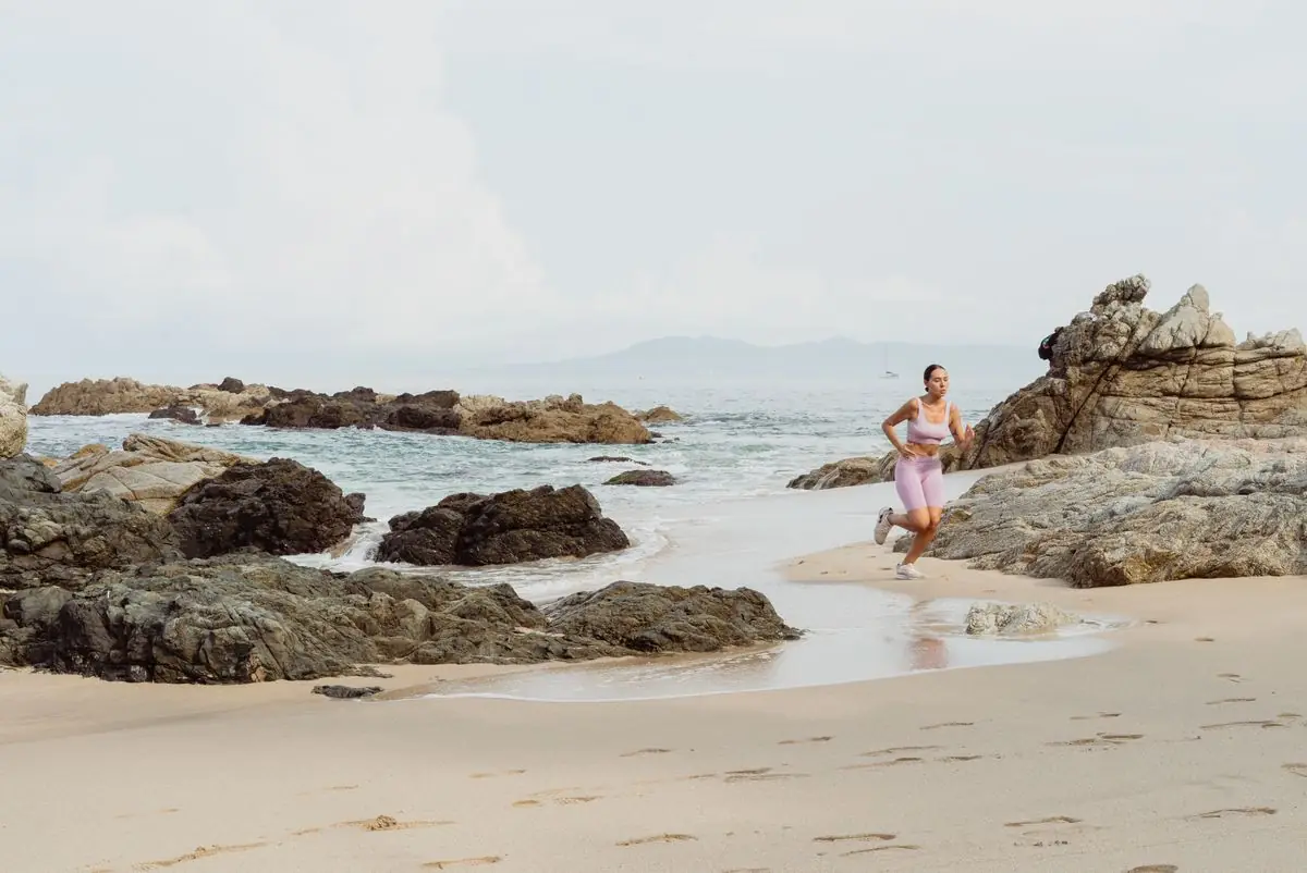 Female athlete jogging along a rocky beach.