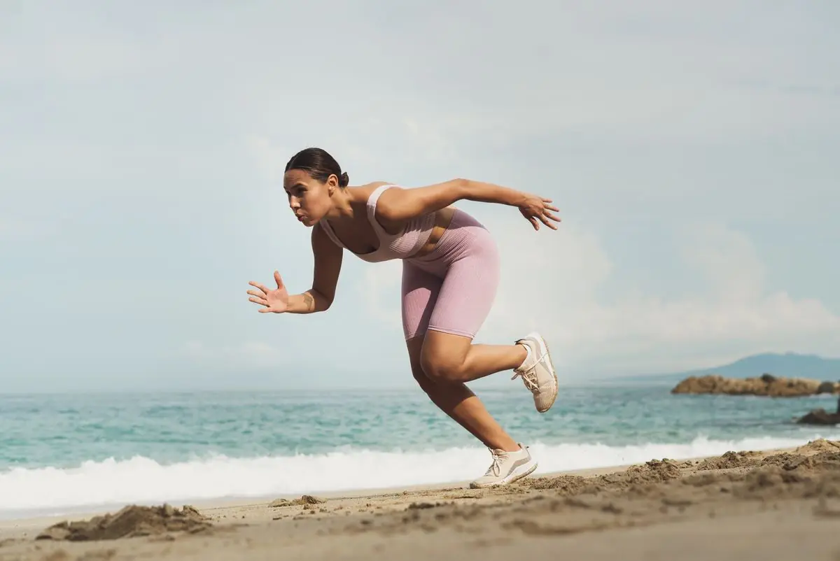 A woman in sportswear running on a sunny beach.