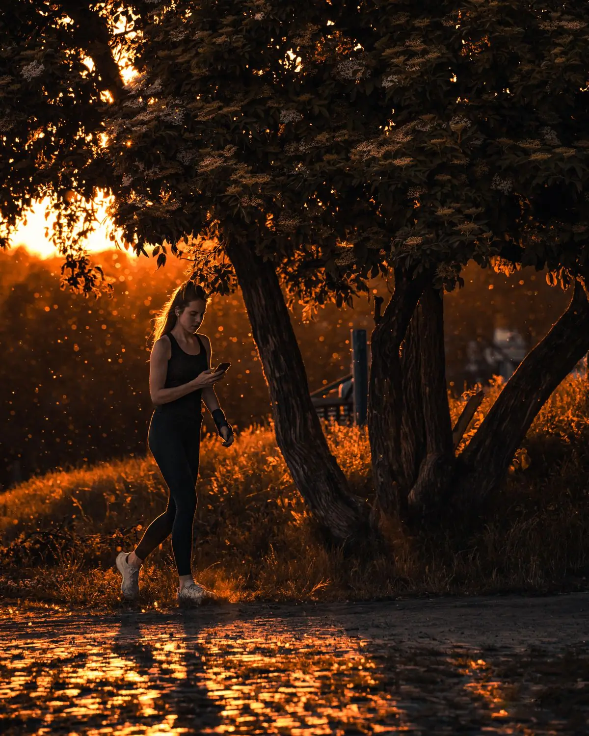 A woman jogging through a sunlit park in Warsaw during sunrise.
