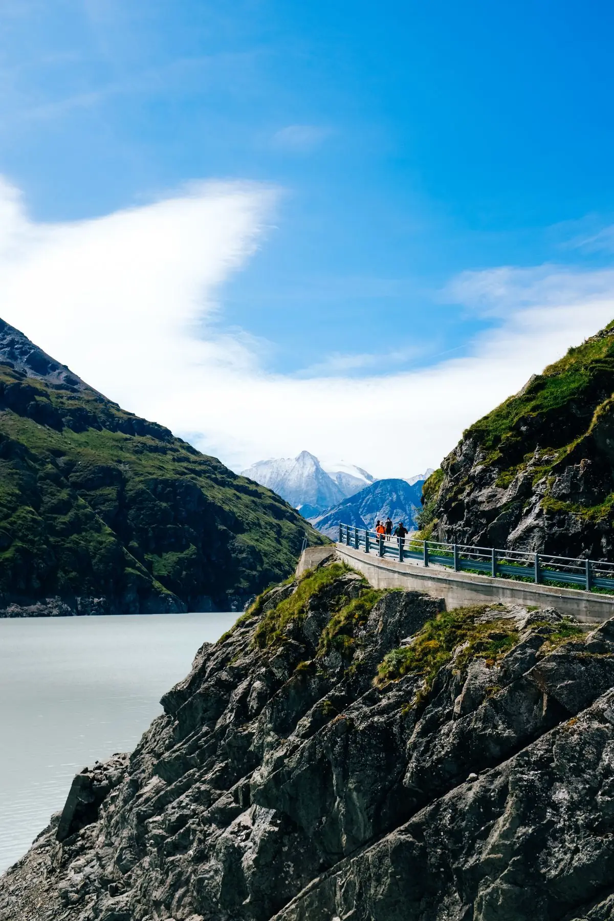 Breathtaking view of a mountain trail with runners and a majestic river under a clear blue sky.