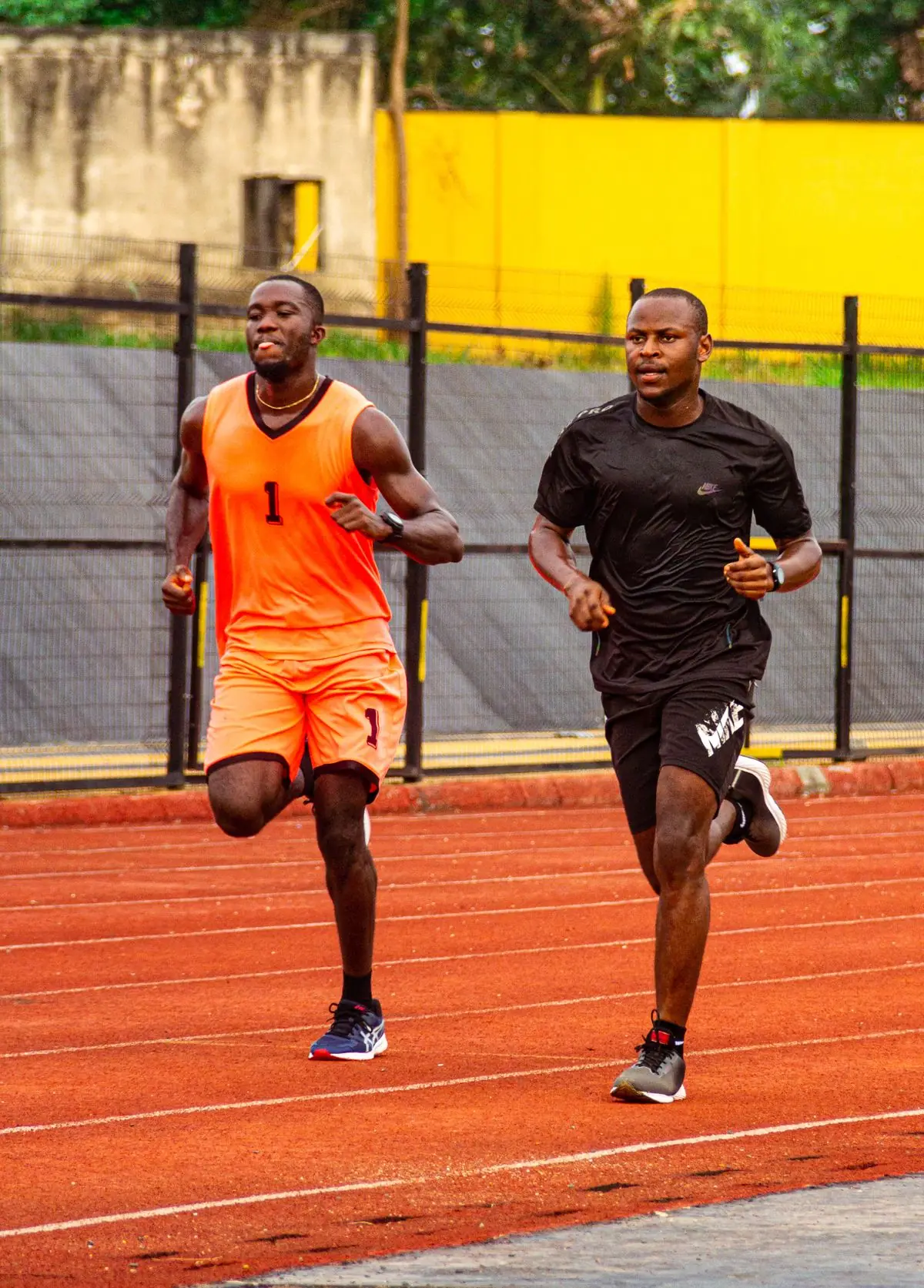 Two adult male athletes sprinting on an outdoor track in sportswear.