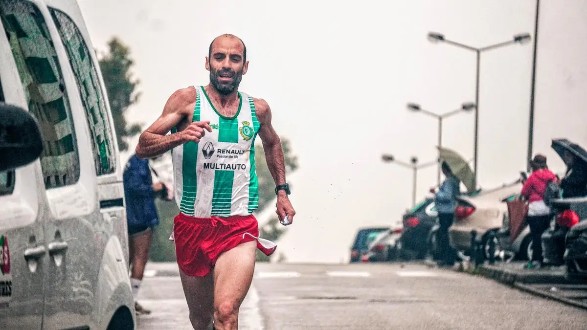 Focused male athlete running a marathon on a rainy city street.