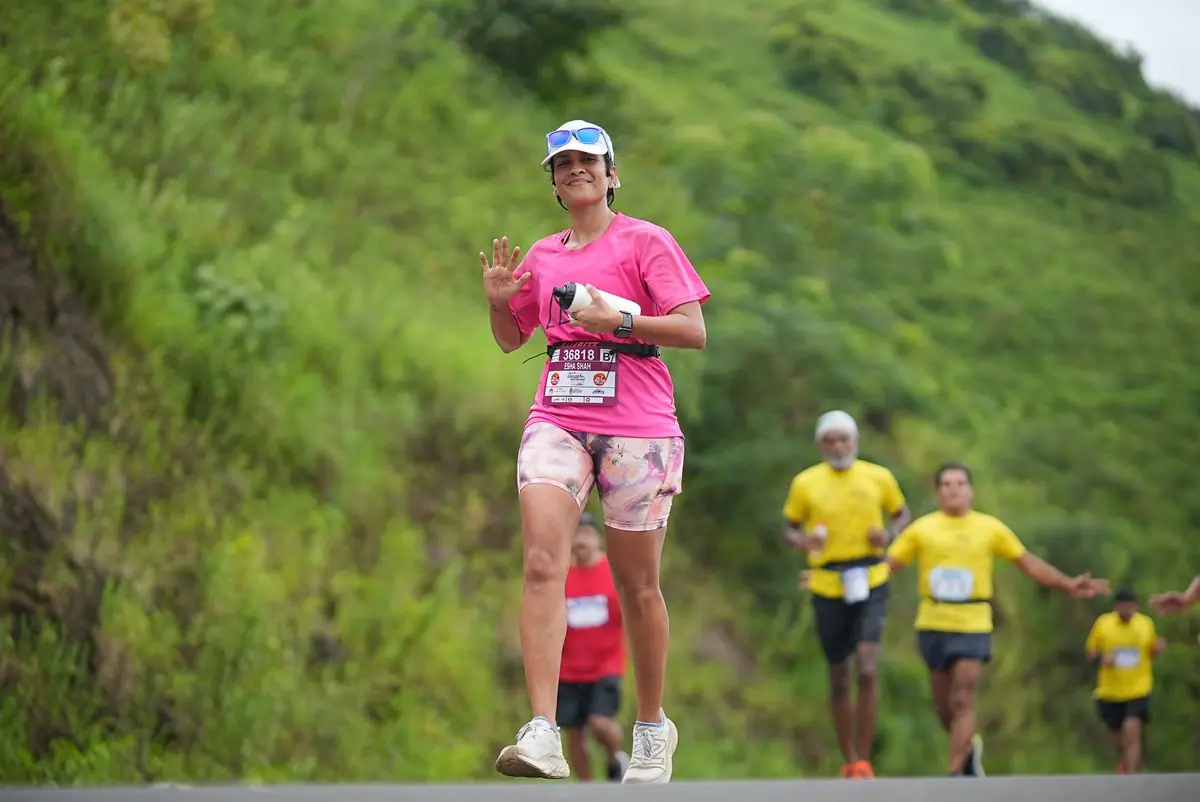 A woman in a pink outfit running a marathon amidst lush greenery.