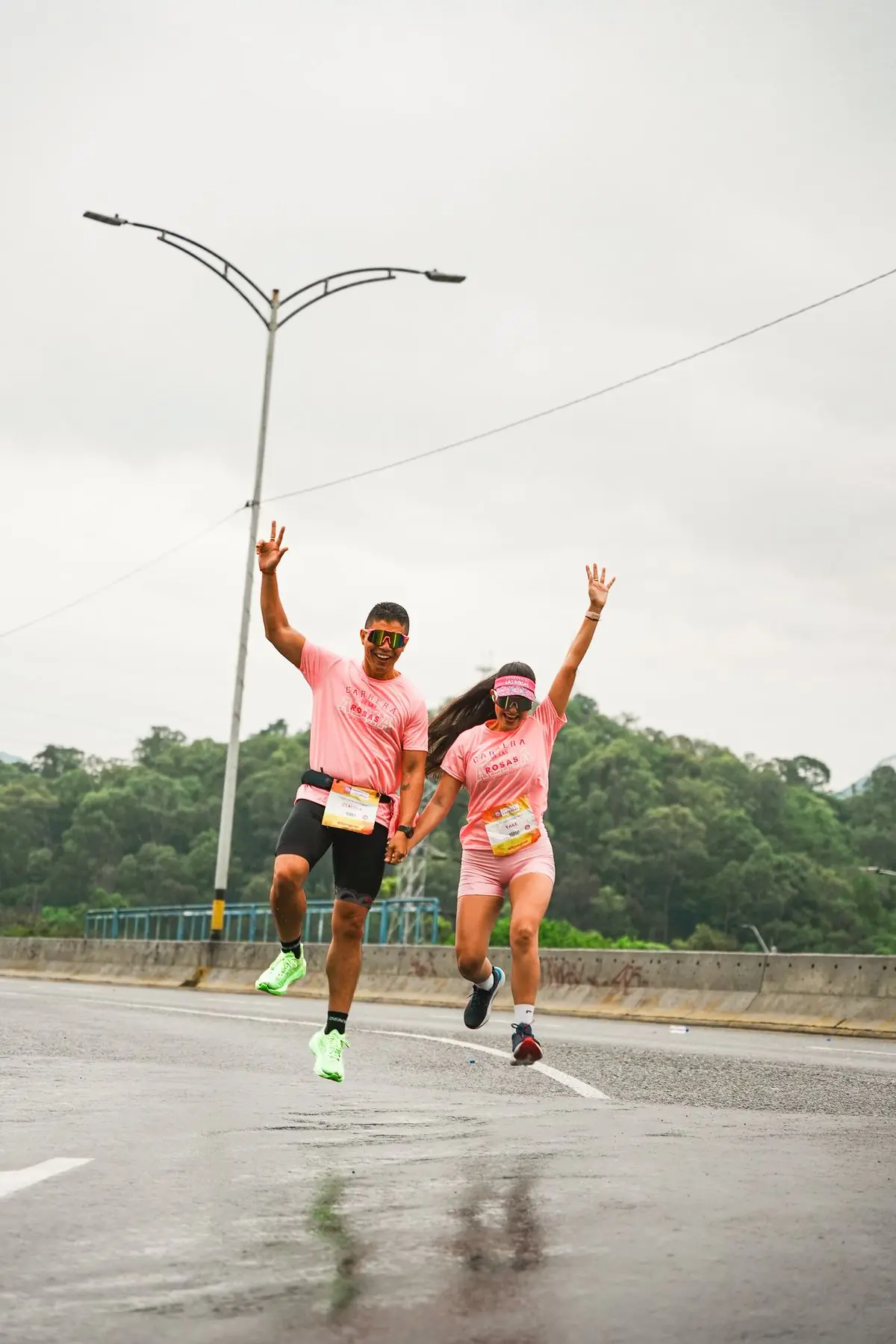 Two athletes in pink outfits joyfully running on a wet road after rainfall.