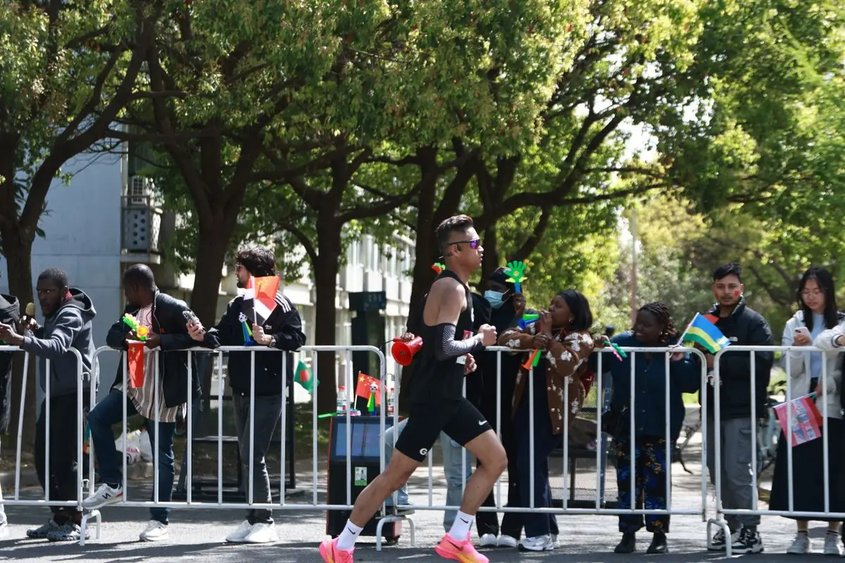 Runner in black racing past cheering crowd at outdoor marathon event.