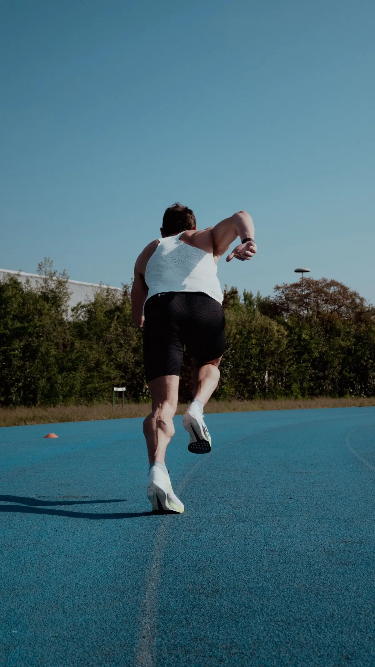 Male athlete starting a sprint on a blue outdoor track under a clear sky.