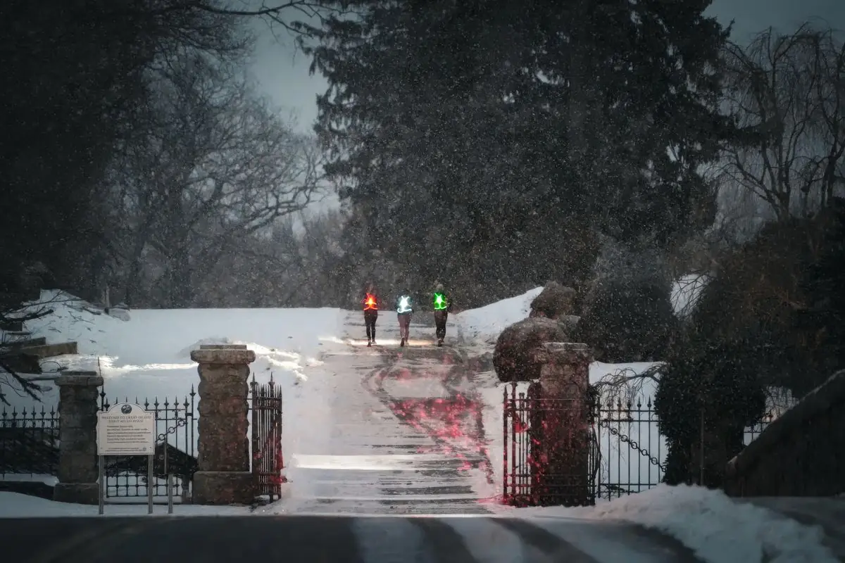 Three joggers in reflective gear running through a snowy park in winter.