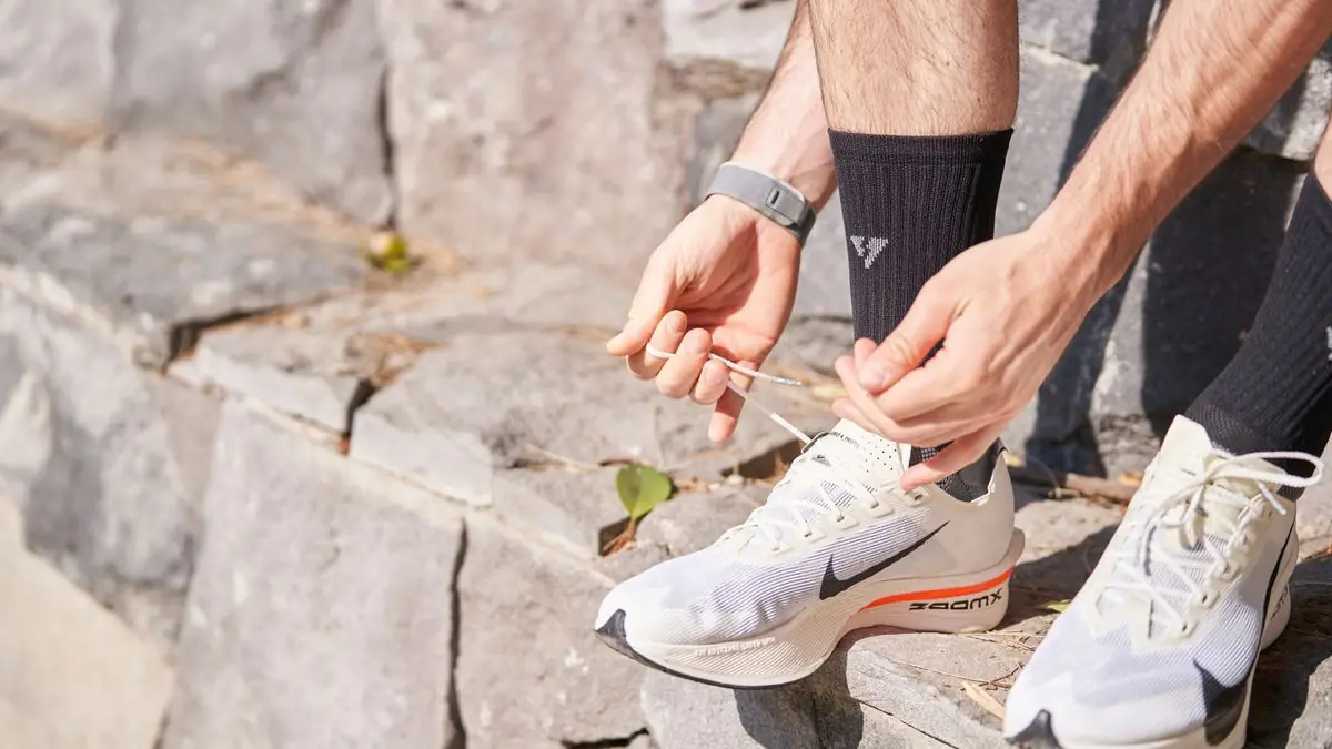 Close-up of a man tying laces on running shoes while sitting on stone steps outdoors.