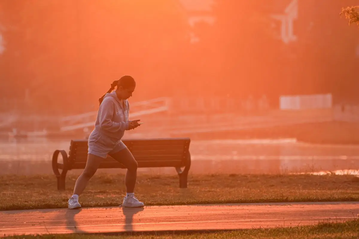A woman jogs along a scenic park trail at sunrise.