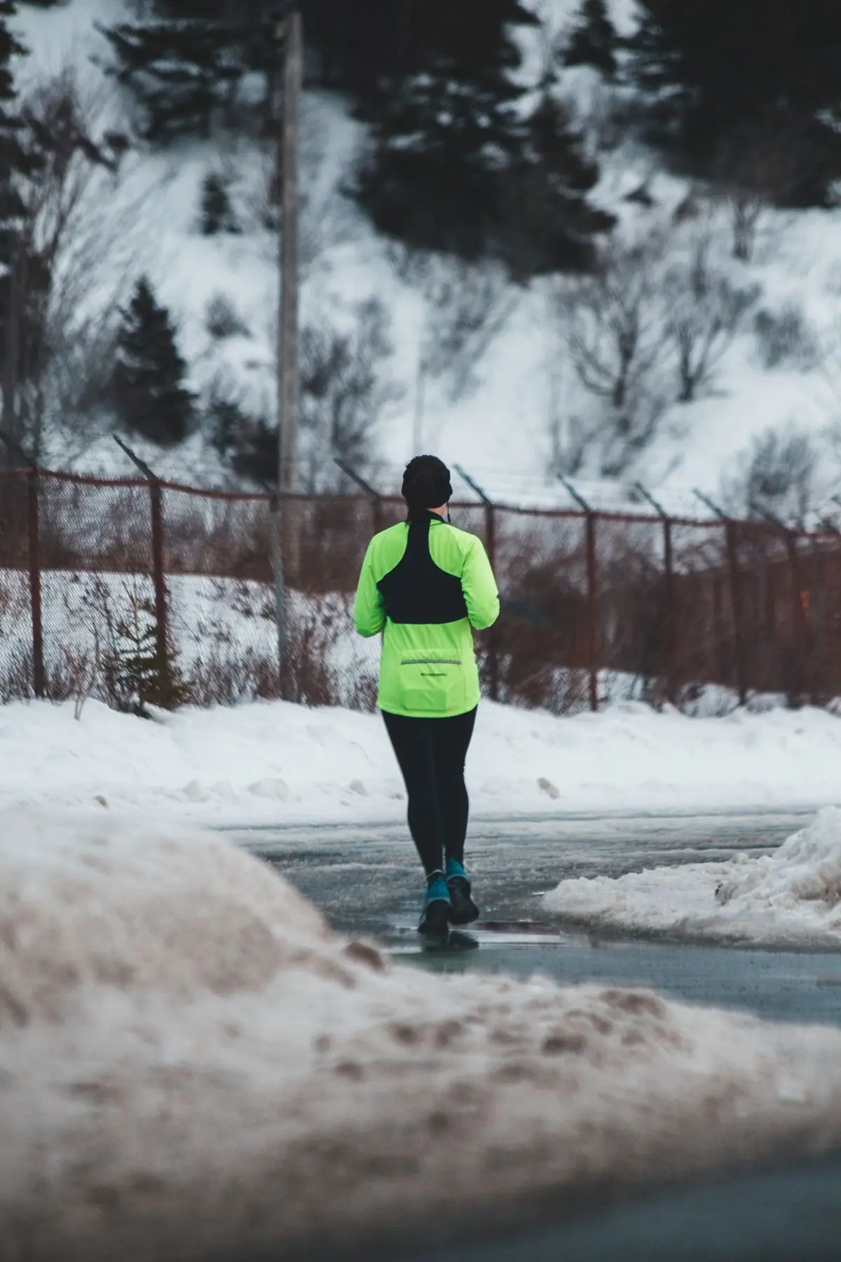 Person jogging in winter wearing bright gear on a snowy path.
