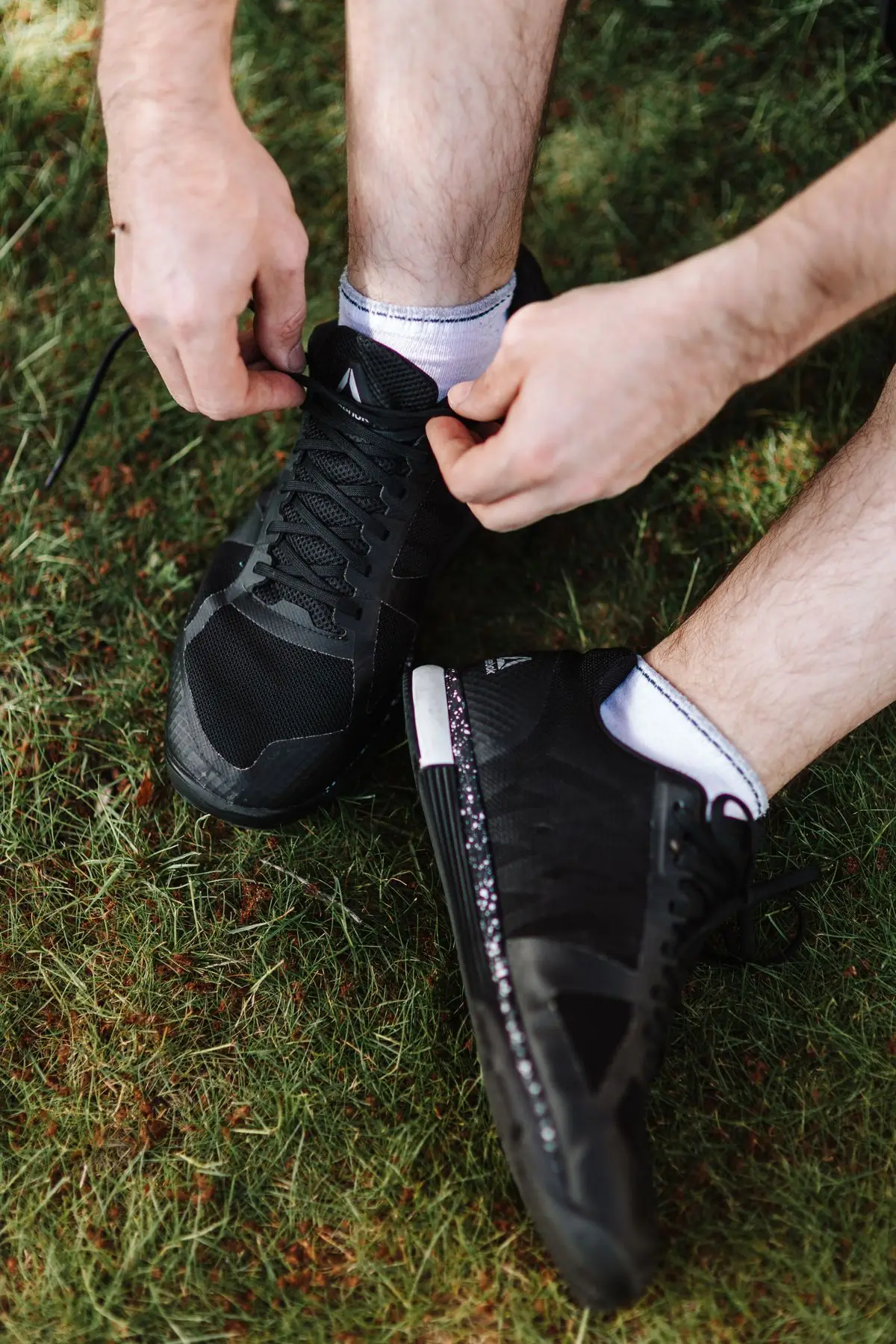 Hands tying the laces on black sports shoes outdoors on grass.