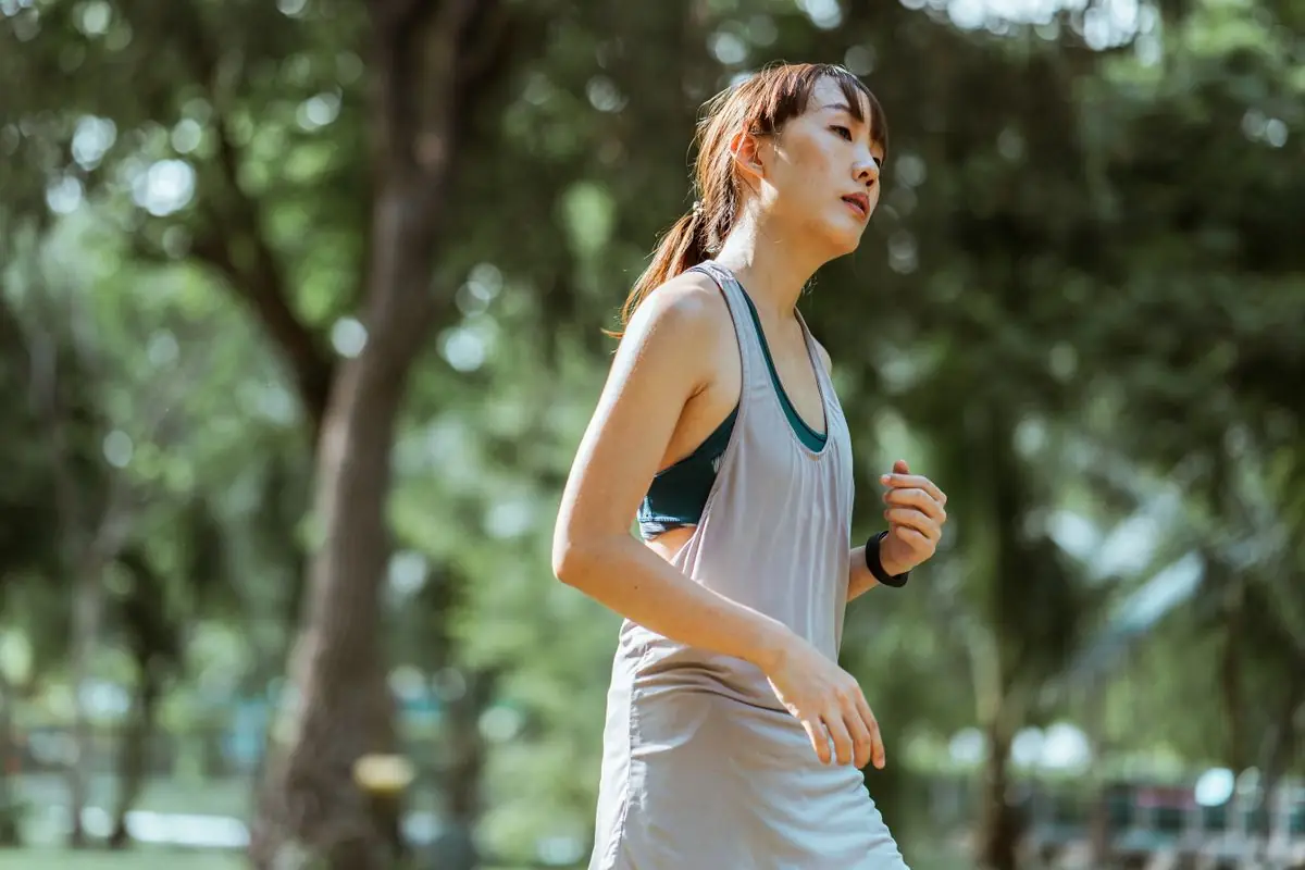 Determined tired female jogger in sportswear running in green park during sunny summer day.