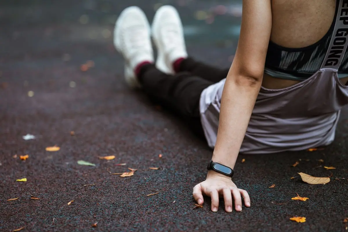 Anonymous female in sportswear and smart watch resting after exercising on sports ground.