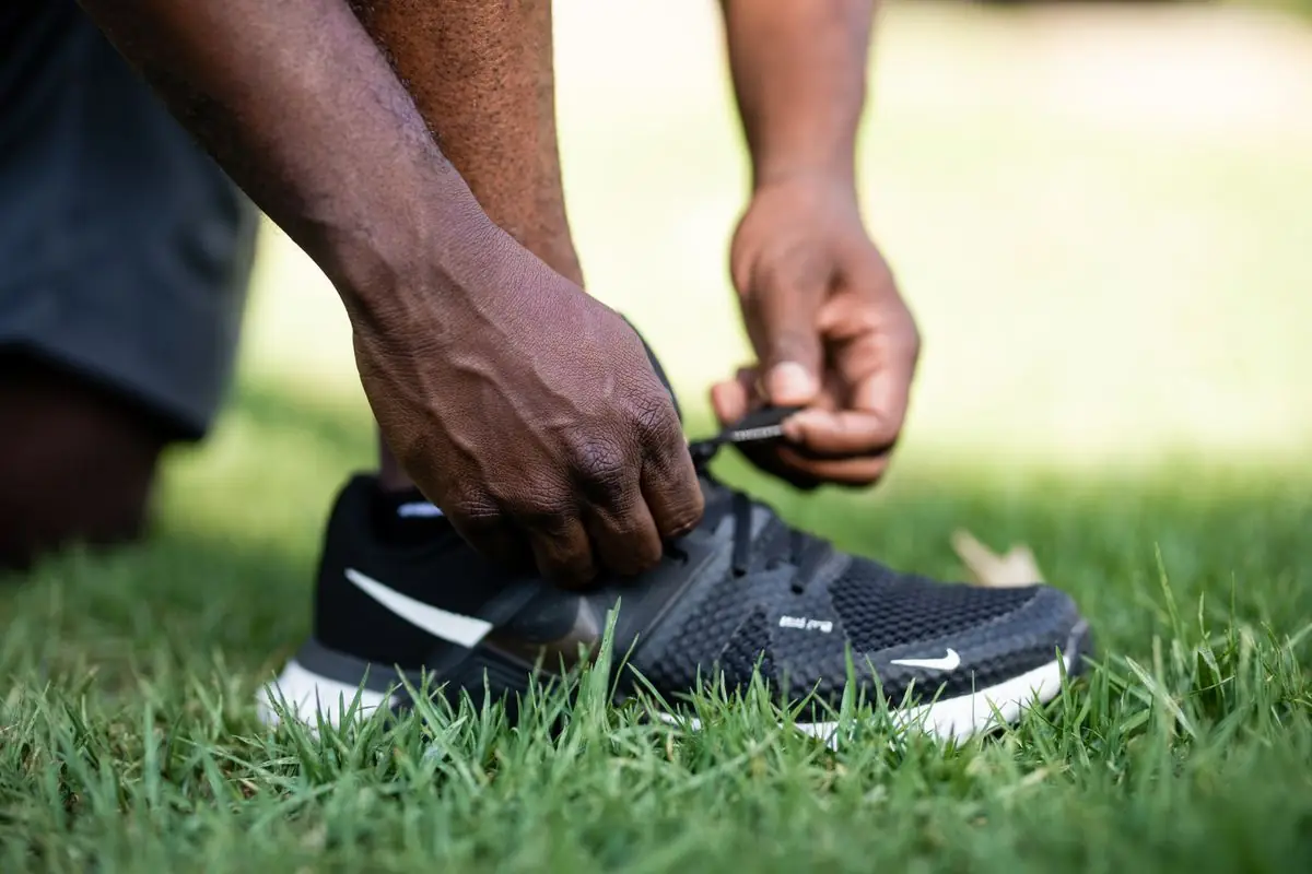 Close-up of a person tying the laces on a black running shoe on grass.