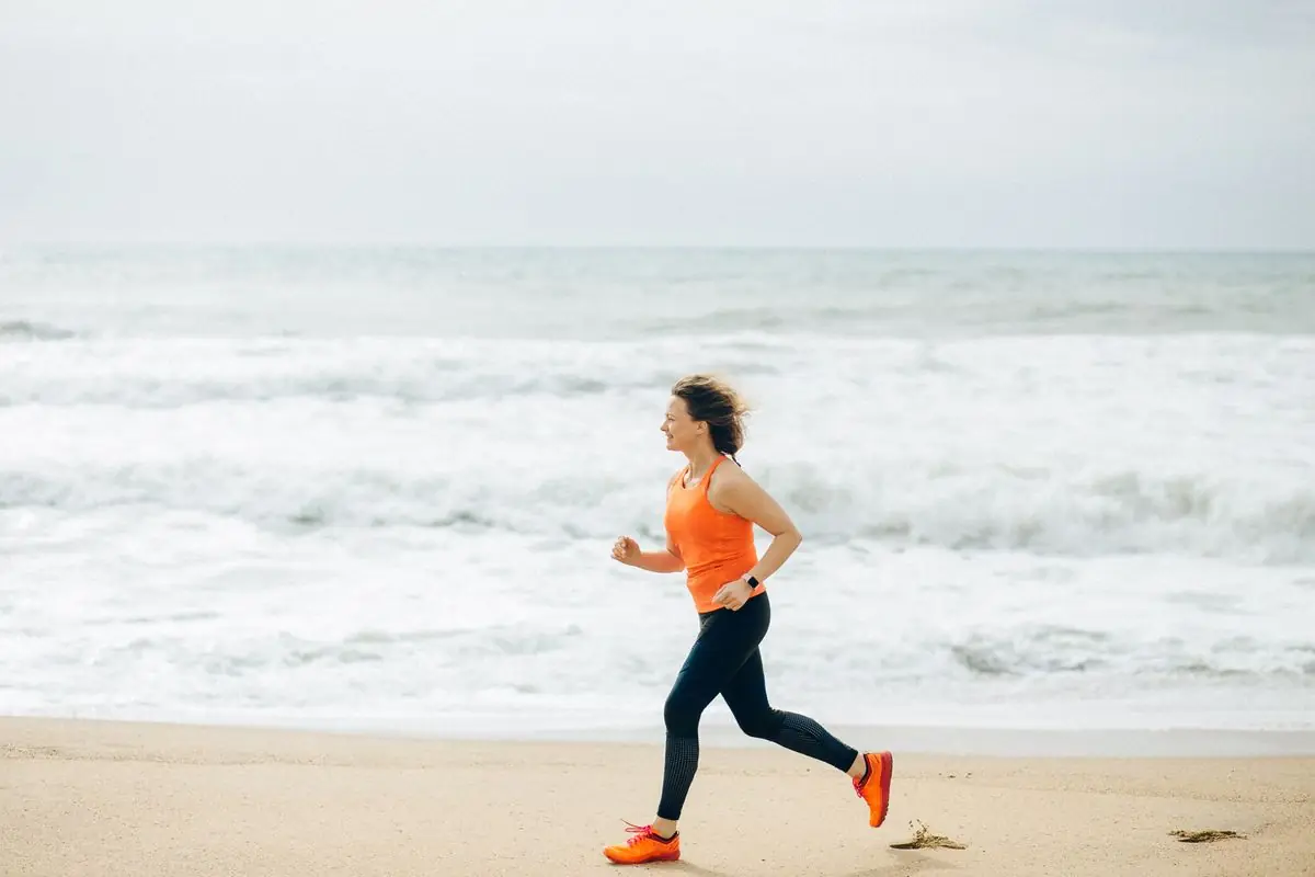 Fit woman running on the sandy beach by the ocean.