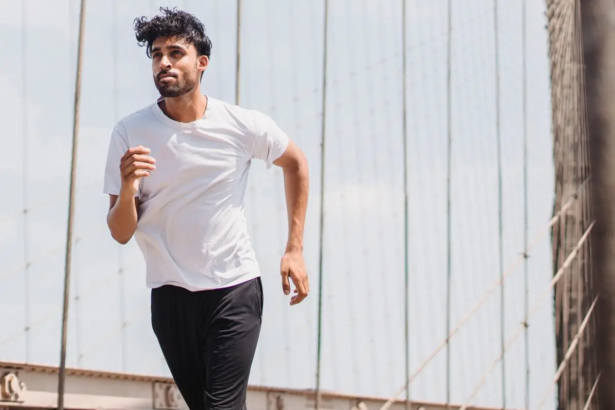 Active young man jogging on a suspension bridge in an urban setting.