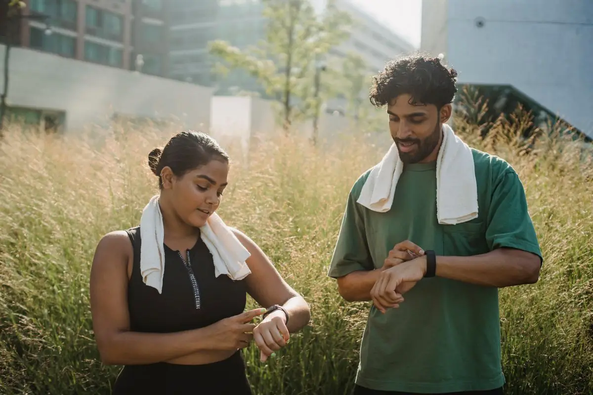 A couple checks their smartwatches after a workout session in a city park.