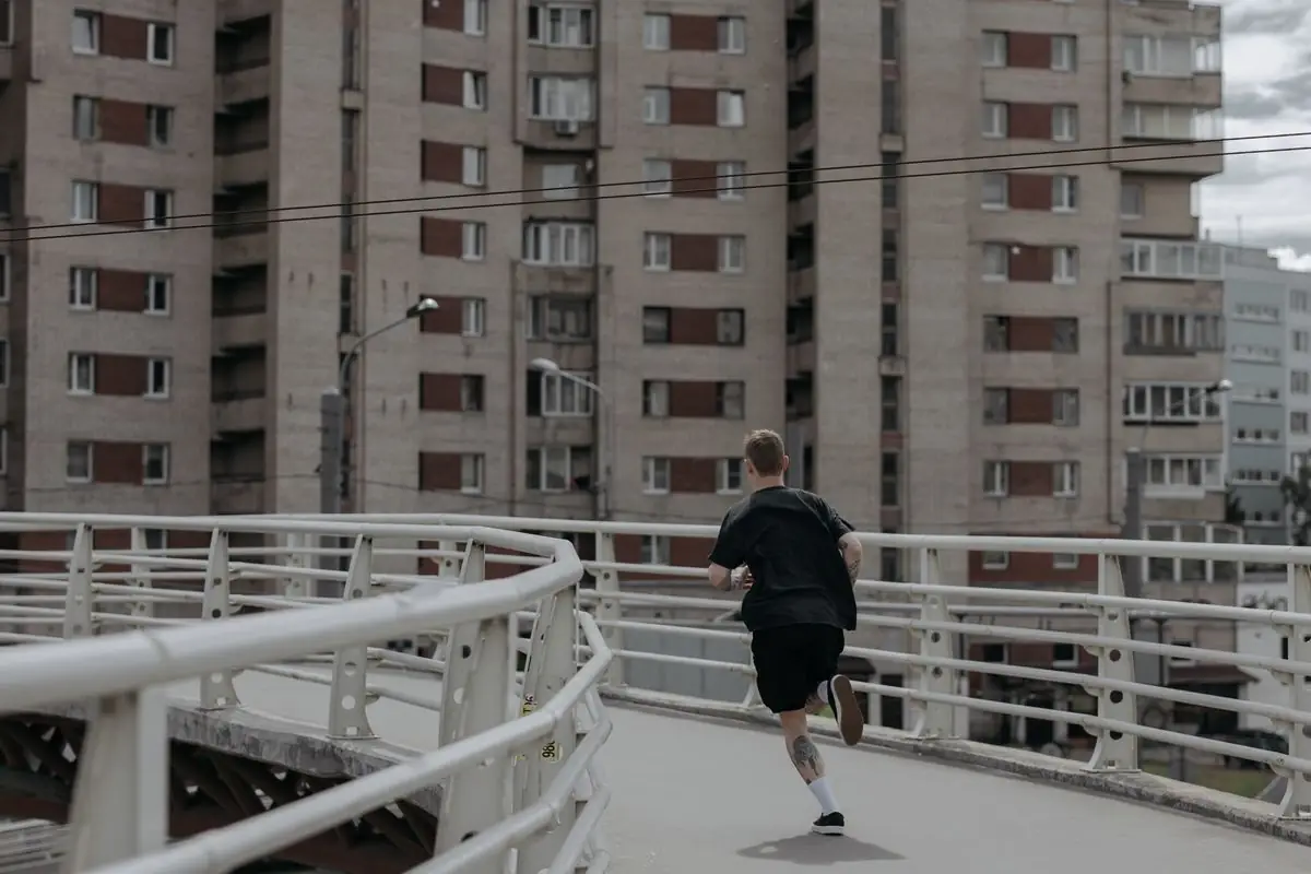 A man running on a footbridge in an urban city setting.