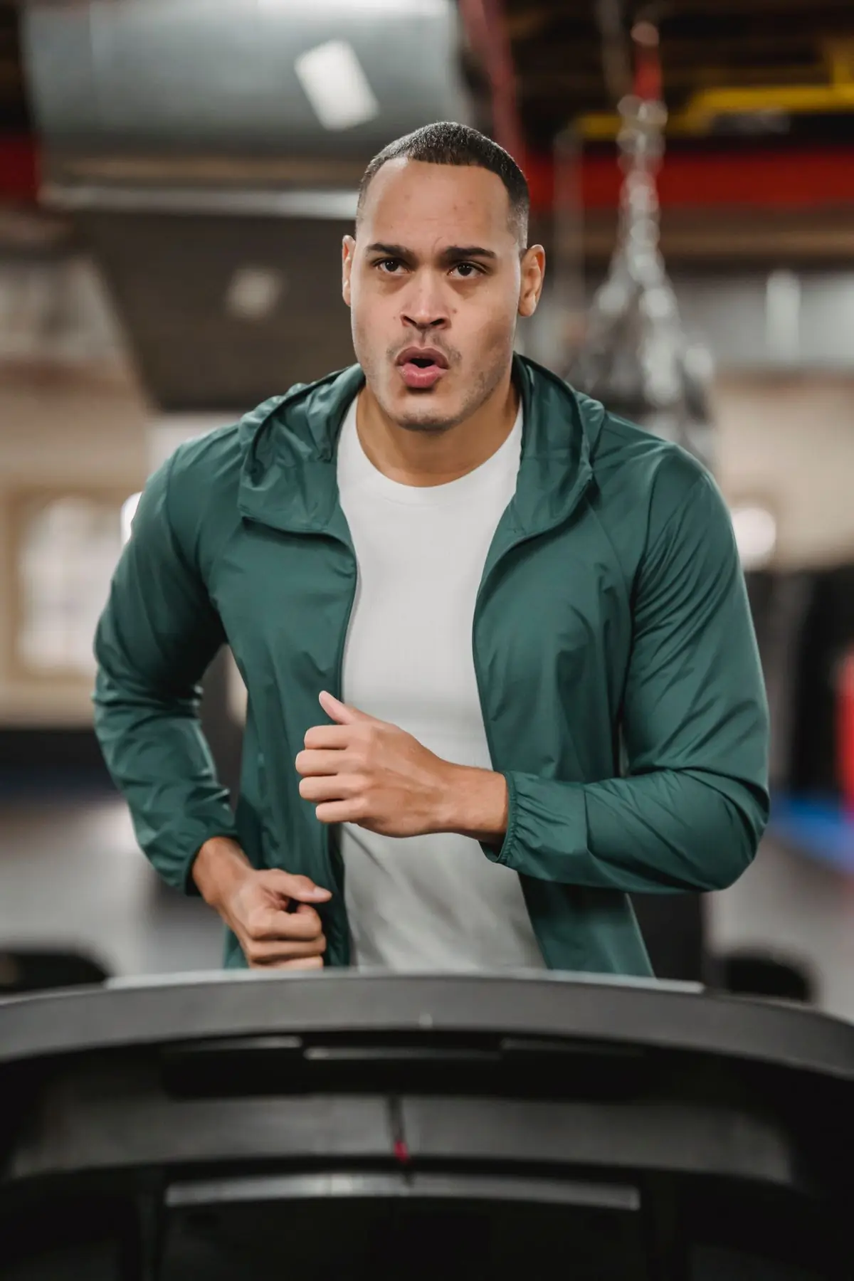 Serious male in sportswear jogging and breathing on modern treadmill on blurred background of gym.
