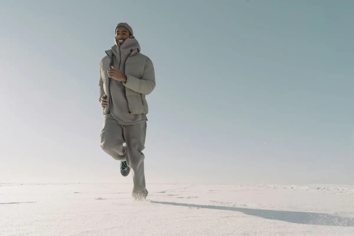 A man in a puffer jacket runs outdoors on a snowy day highlighting fitness and winter fashion.