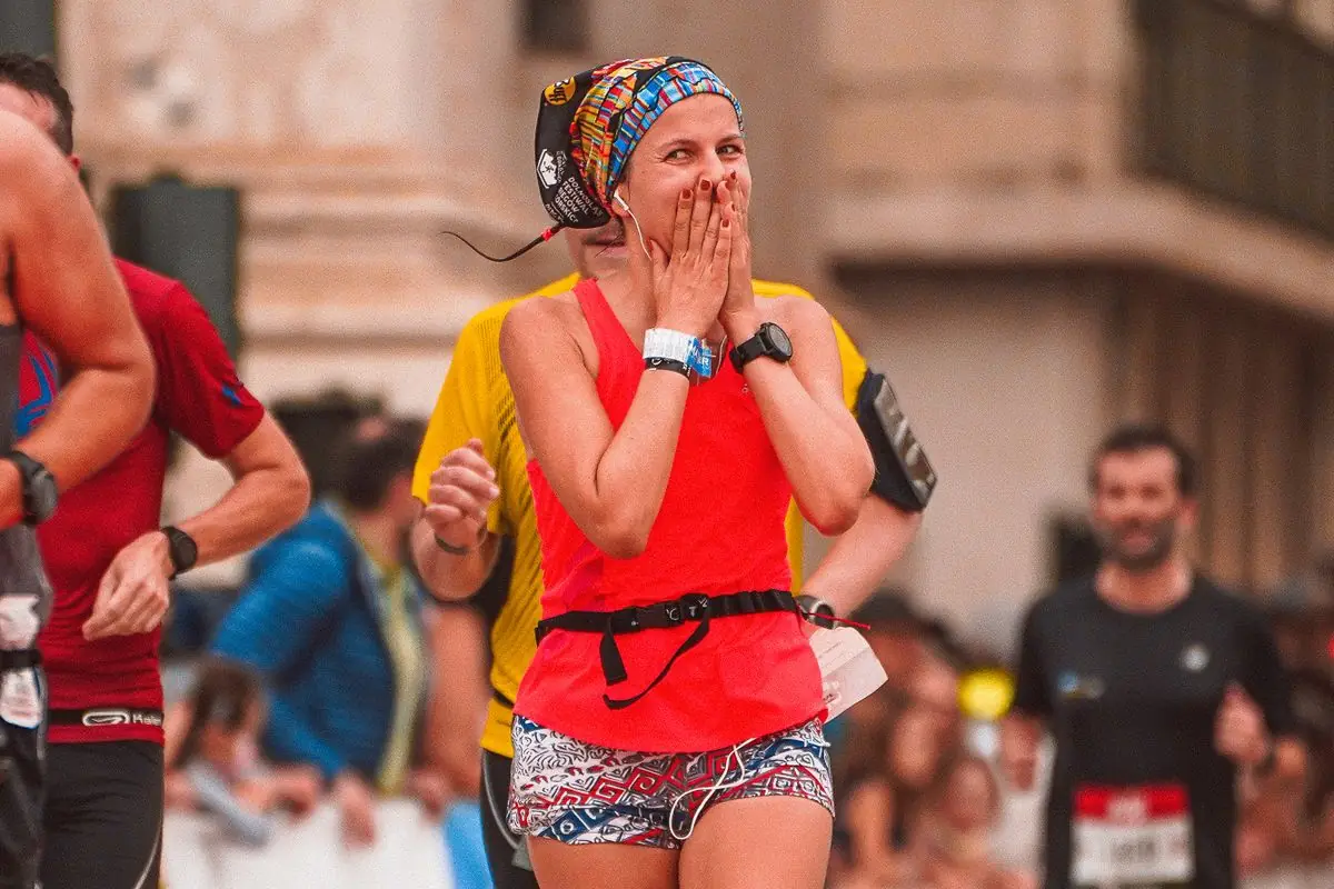 Elated woman celebrates finishing a marathon surrounded by fellow runners.