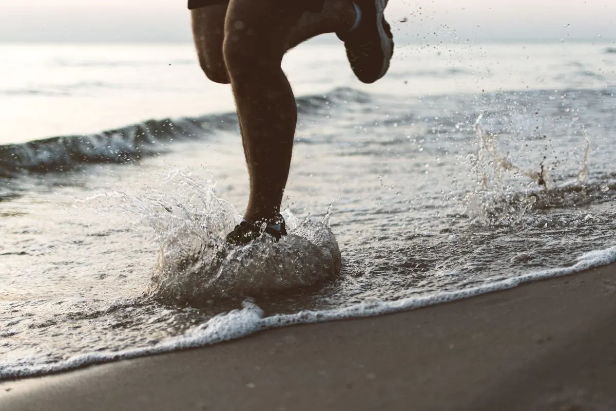 A runner’s shoes splashing through the water at the shoreline